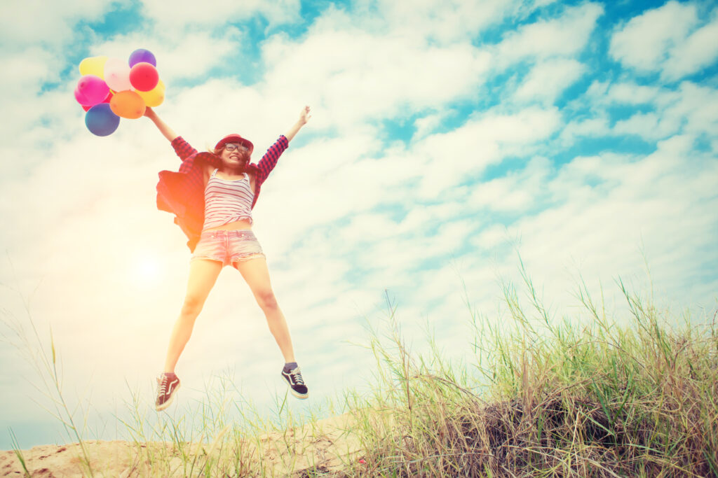 Mädchen springt freudig in die Luft und hält dabei Ballons in der Hand